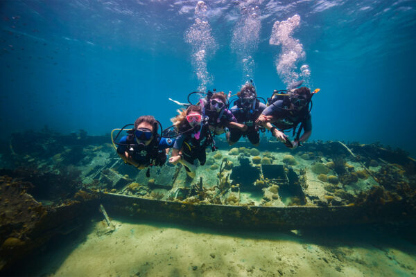 dive divers link arms underwater in front of a wreck in curacao