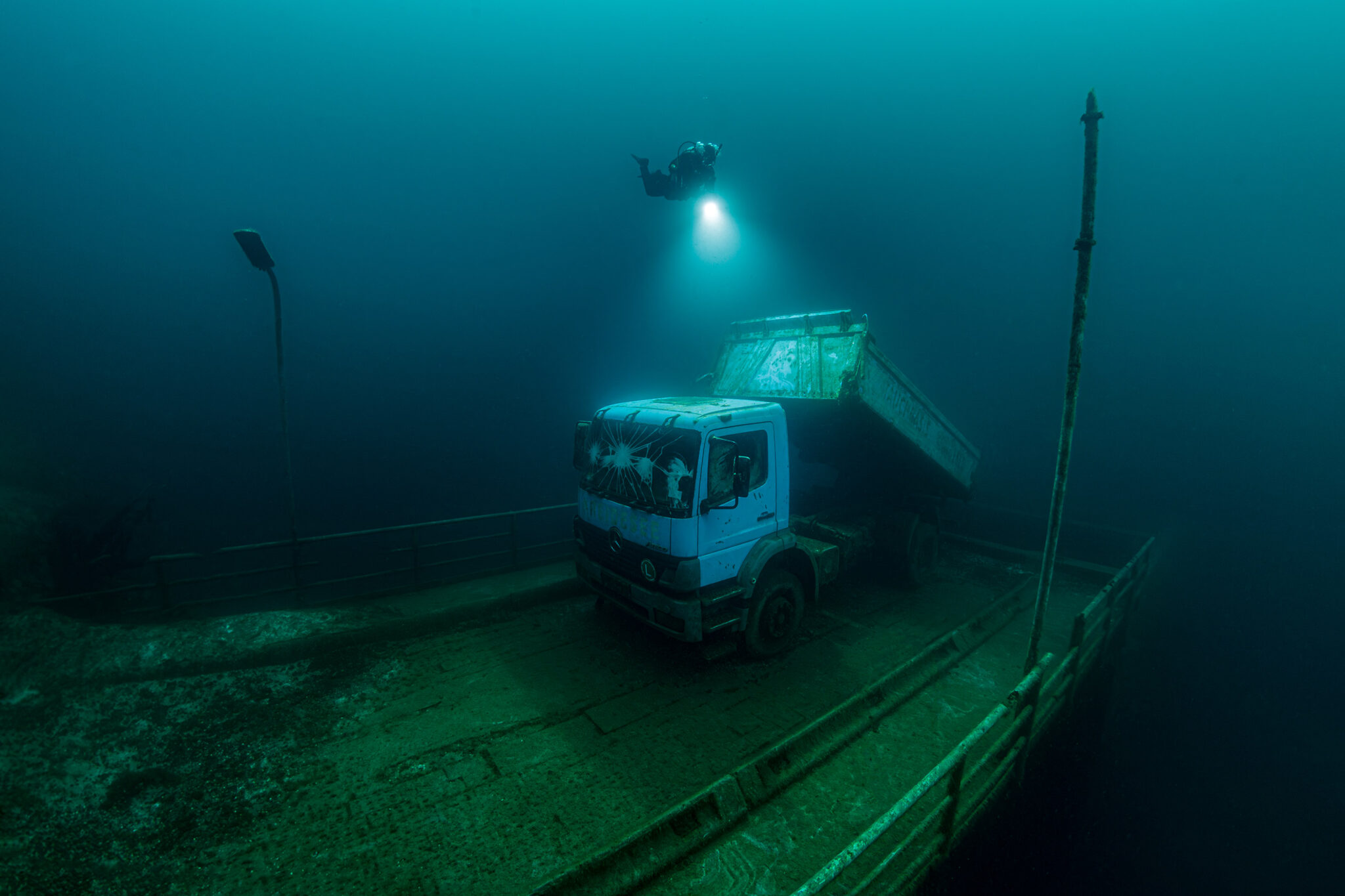 A diver shines a flashlight on a truck that was sunk in a quarry in Germany to make an artificial reef