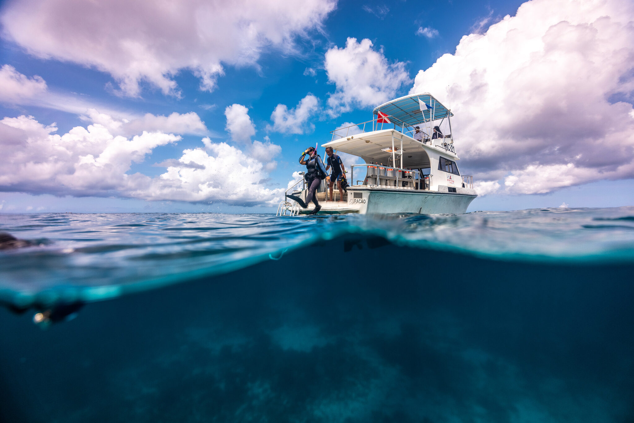 two divers prepare to take a giant leap off the back of a dive boat
