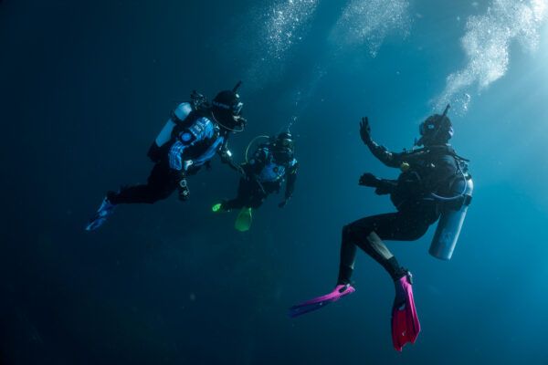 A scuba diving instructor signalling "ok" underwater to two other divers.