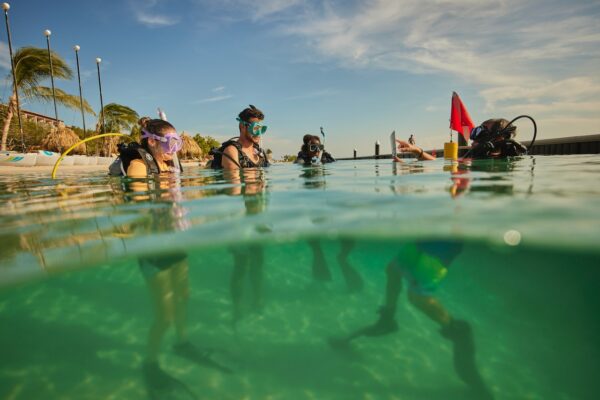 A scuba diving instructor teaches three new divers in shallow water near a beach in Curacao