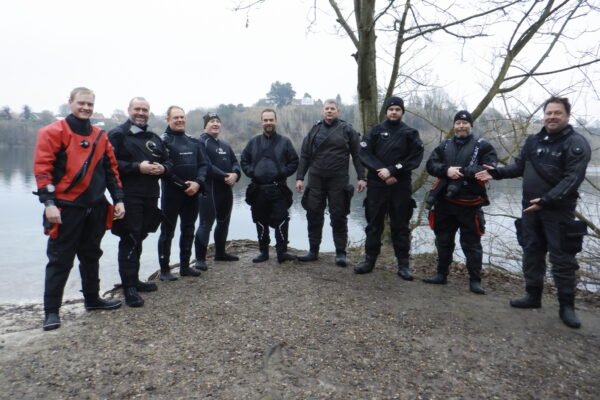 diving as therapy advocates stand on the edge of a cold lake in dive gear