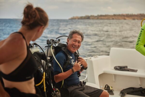 A diver smiles at another diver while gearing up to go scuba diving on a recreational dive boat.
