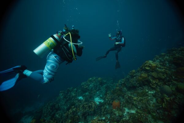 An instructor looks back on a scuba diving student as they dive over a coral reef in Curacao