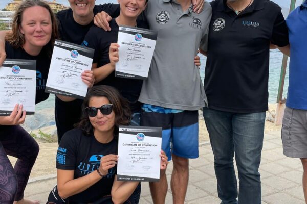A bunch of smiling people huddle together and hold up certificates. They've just become PADI Pros.