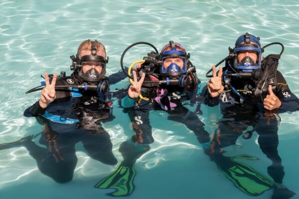 padi ceo poses in a full face mask in a swimming pool with two other divers