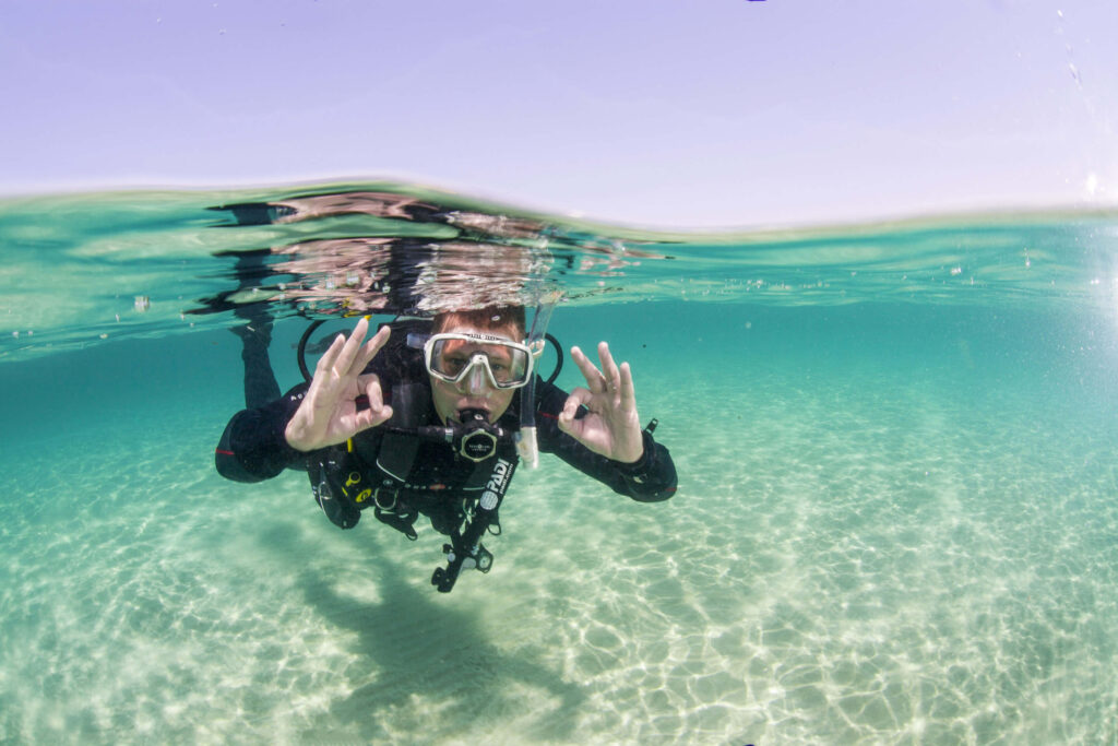 A beginner diver takes his first breath in the water and gives the okay sign with both hands.