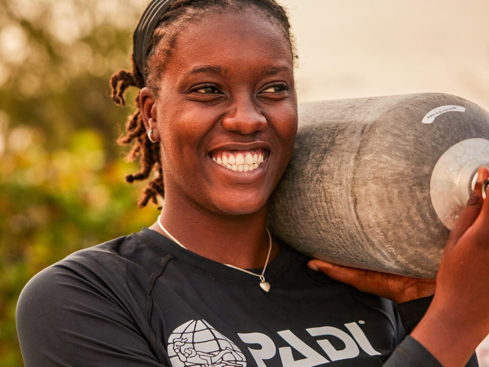 female diver smiling and carrying a scuba tank