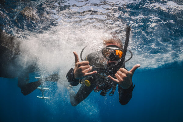 a man gives two shaka signs just after jumping in the water to go scuba diving