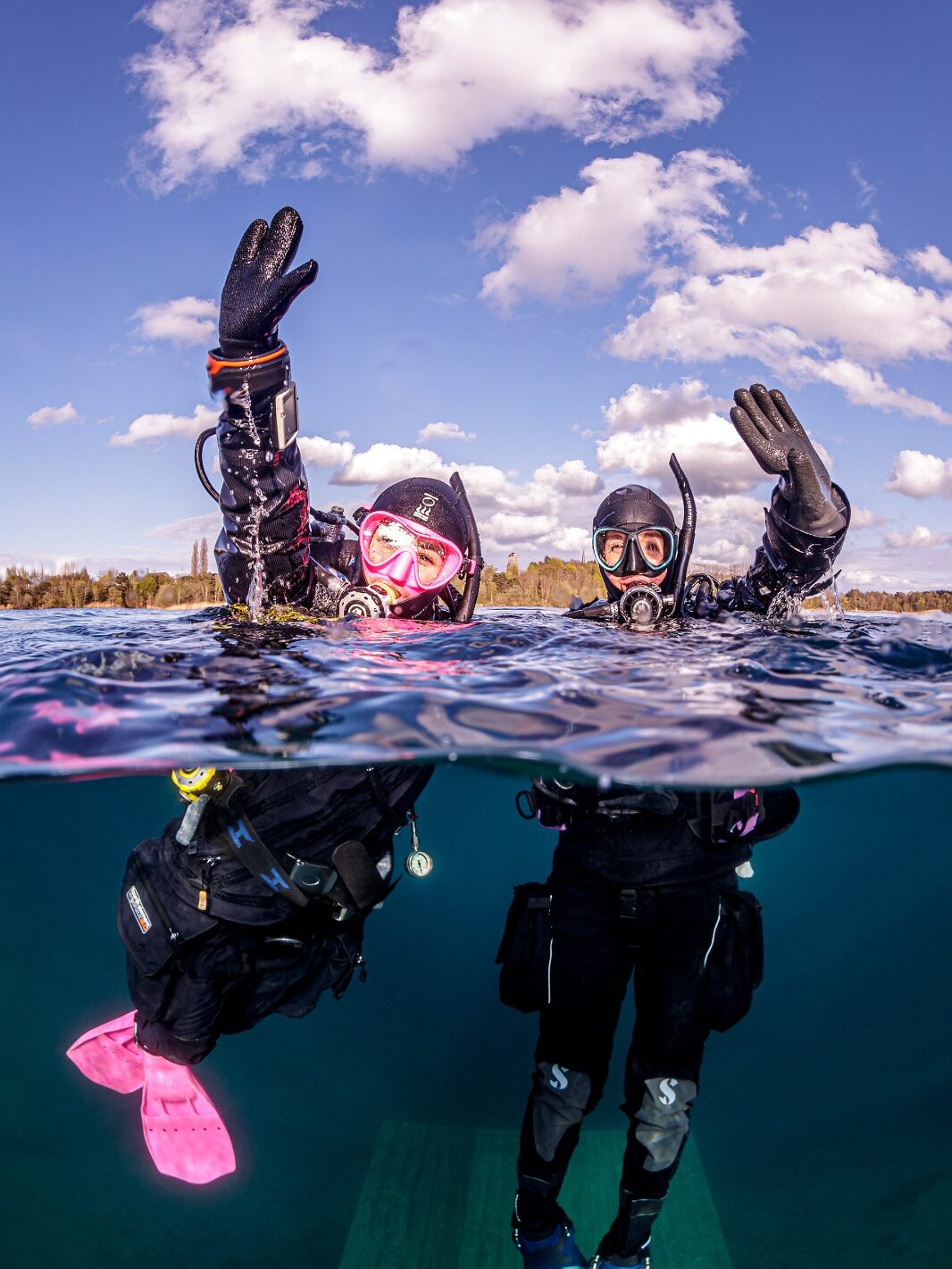 two in-water divers with their hands in the air