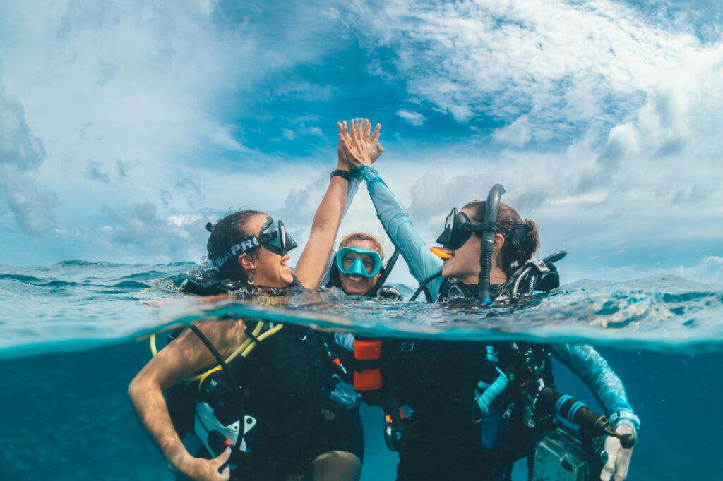 two female divers give each other a high five at the surface after a great dive