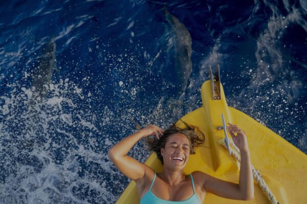 happy woman on the boat accompanied by dolphins in the sea
