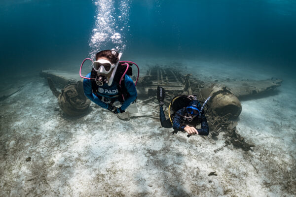 two divers swim away from an underwater airplane in the Bahamas