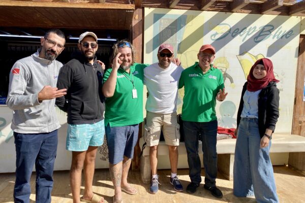 A group of people from Aqaba Jordan and Green Fins smile for the camera in front of a PADI dive center