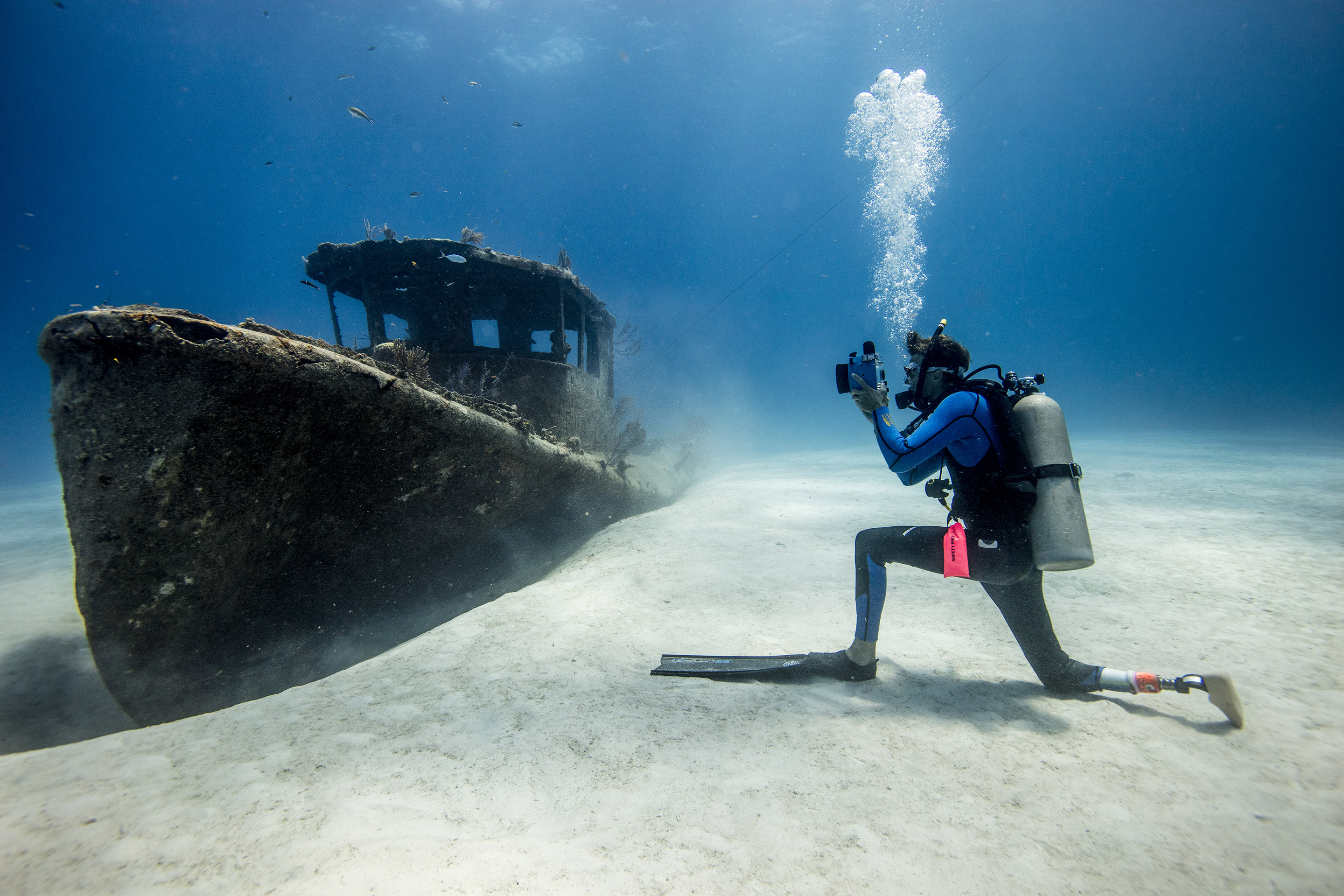 Buceador con una pierna ortopédica arrodillado en la arena para hacer una foto del pecio