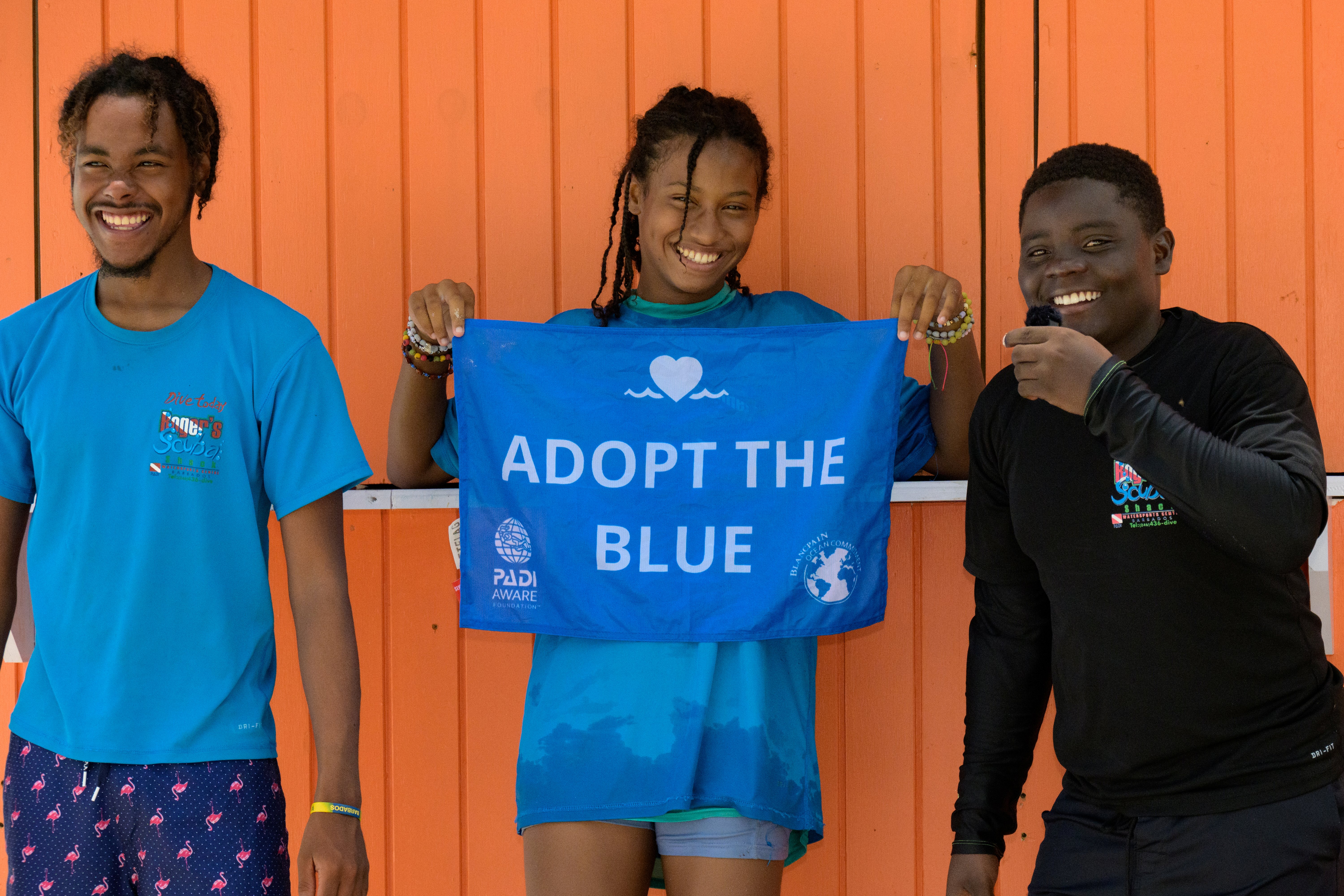 Three divers smiling holding an Adopt The Blue flag