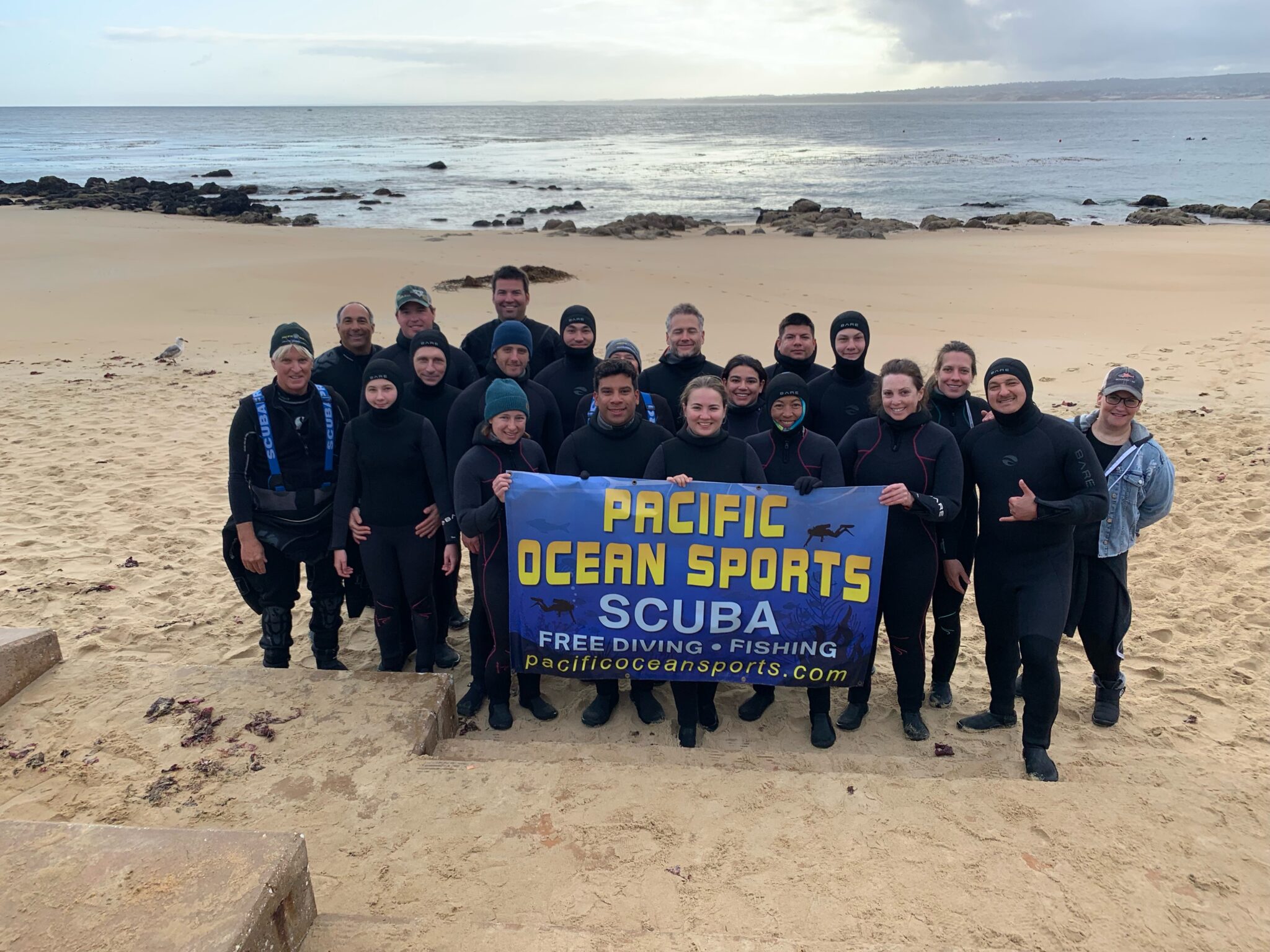 Group photo of divers on a beach holding a flag for Pacific Ocean Sports- winner of MSD Challenge 2025
